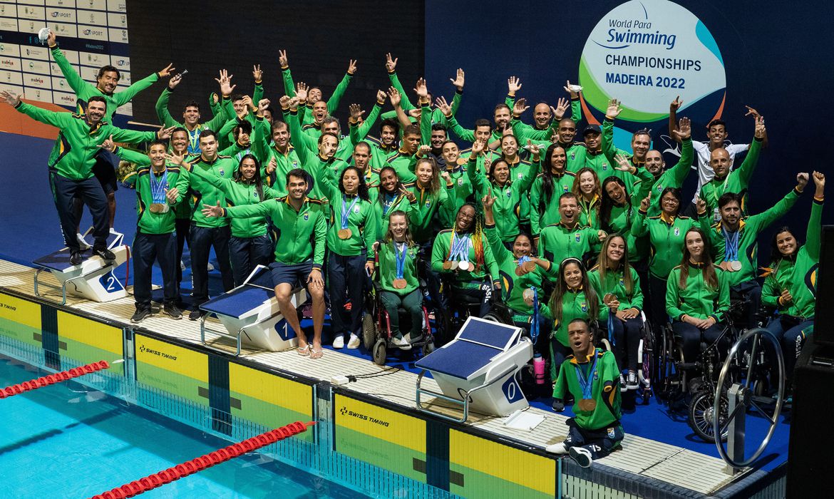 Os resultados sinalizaram que o Brasil precisaria ir além de seus maiores nomes para seguir em alta. Os Jogos de Tóquio deram a resposta: cinco atletas diferentes responsáveis pelas oito medalhas douradas na capital japonesa, o dobro do amealhado no Rio de Janeiro, em 2016, quando somente Daniel conquistou ouros (quatro). Carol e Wendell voltaram ao topo, agora na estreia paralímpica de ambos, sendo que a velocista da classe S12 (baixa visão) esteve lá três vezes. Na segunda Paralimpíada da carreira, Talisson Glock ficou com o ouro pela primeira vez. Revelados após o Mundial, os “Gabrieis” Araújo e Bandeira também debutaram com estilo no evento. Já no Mundial deste ano, o Brasil teve 15 campeões entre os 29 integrantes da delegação que viajou a Portugal, sendo sete em provas individuais: Carol Santiago, Cecília Araújo, Gabriel Araújo, Gabriel Bandeira, Gabriel Cristiano, Mariana Gesteira e Samuel Oliveira. Apenas três dos nadadores retornaram ao Brasil sem medalhas. Ou seja: quase 90% dos brasileiros estiveram no pódio em Funchal. O detalhe é que a pluralidade de ouros (19 ao todo) não impediu que o Brasil seguisse com seus multimedalhistas. Carol, por exemplo, foi ao pódio sete vezes, seis delas no topo. Os “Gabrieis” Araújo e Bandeira, além de Samuel, levaram cada um três láureas douradas, enquanto Mariana ganhou outras duas. Os campeões da Ilha da Madeira também simbolizam presente e futuro da natação paralímpica brasileira, que foi para o Mundial com mais de um terço (35%) da delegação formada por nadadores com menos de 23 anos, seguindo a renovação iniciada em Tóquio. Os dez atletas do recorte foram medalhistas e metade foi ao topo do pódio. Entre eles, Samuel, de apenas 16 anos, que tem brilhado na classe S5 (a mesma em que Daniel Dias competia antes de se aposentar). 4X100M LIVRE REVEZAMENTO S11-S13, mundial de natação paralímpica Delegação brasileira também brilhou nas provas coletivas em Portugal - Ale Cabral/CPB/Direitos Reservados. É verdade que China e Rússia, duas das maiores potências da modalidade, não estiveram em Portugal, ainda que por razões diferentes. Os chineses não costumam disputar o primeiro dos dois Mundiais do ciclo, mas devem marcar presença no do ano que vem, em Manchester (Grã-Bretanha). Já os russos estão suspensos pelo Comitê Paralímpico Internacional (IPC, sigla em inglês), devido à invasão militar à Ucrânia. Ainda assim, o Brasil deu, sim, um salto em relação a Tóquio, superando britânicos e australianos (que ficaram à frente na Paralimpíada) no quadro de medalhas do Mundial. Já no total de pódios (53), os brasileiros ainda obtiveram 13 a mais que os Estados Unidos, que só terminaram à frente pelo número de ouros (24 a 19). Em um ciclo reduzido, impactado pela pandemia do novo coronavírus (covid-19), os resultados na Ilha da Madeira trazem otimismo à natação paralímpica brasileira pensando nos Jogos de Paris (França), em 2024. A prospecção de talentos nas Paralimpíadas Escolares, a maior atenção às categorias de maior comprometimento físico-motor (Gabriel Araújo, por exemplo, é fruto de ambos) e o aumento do protagonismo feminino na seleção explicam o desempenho. Mais plural que nunca, o Brasil deixou o Complexo de Piscinas Olímpicas de Funchal consolidado como potência da modalidade. Edição: Fábio Lisboa